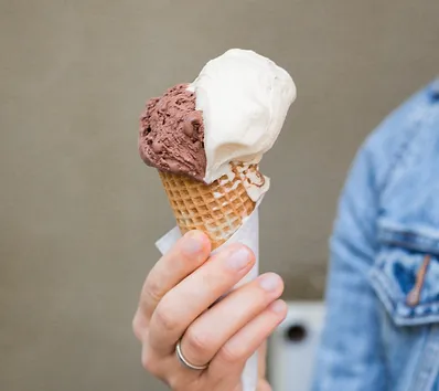 A young hand holding an ice cream cone with both chocolate and vanilla scoops